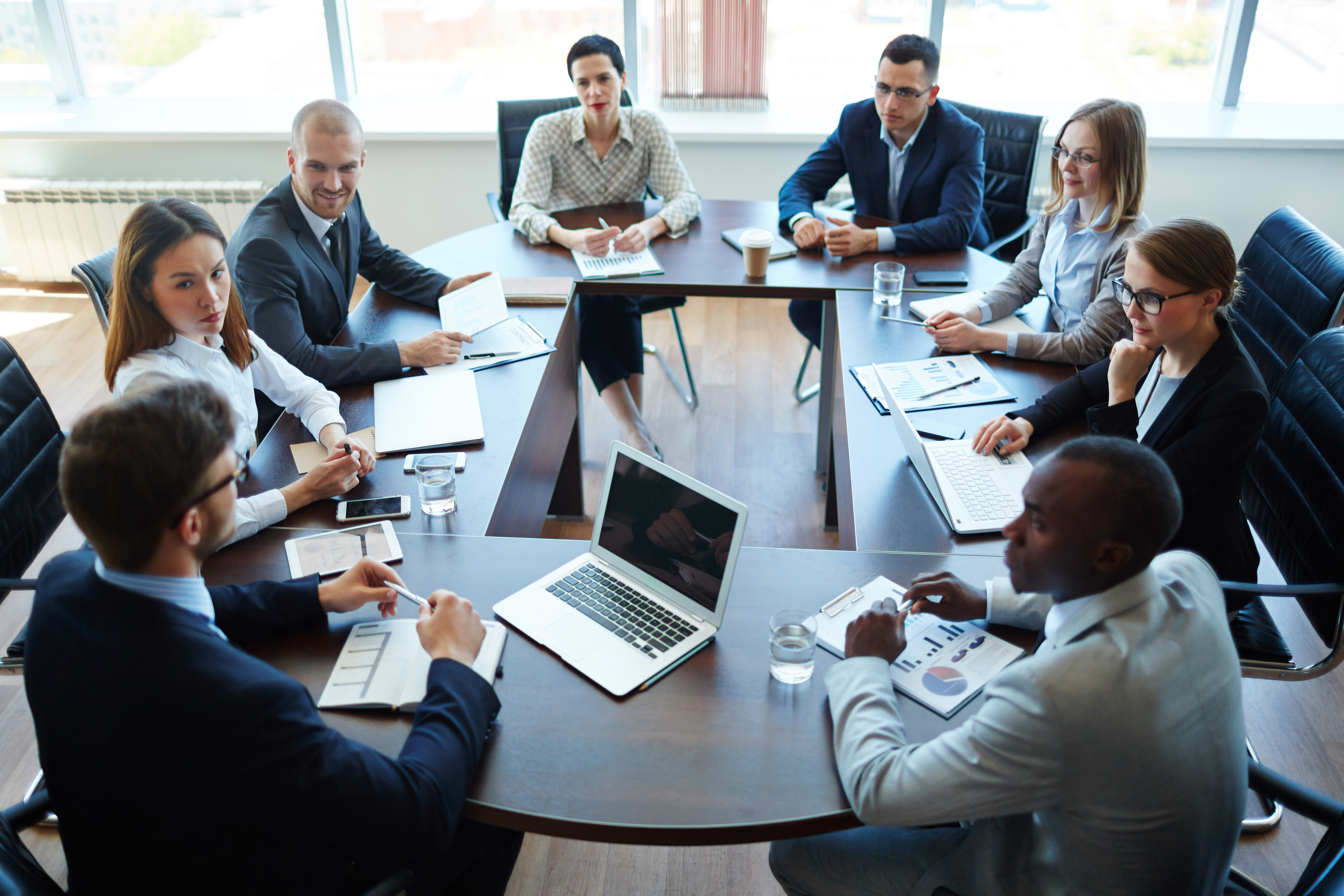 Executive leadership team in a boardroom discussing hiring decisions and reviewing financial performance during a strategic meeting